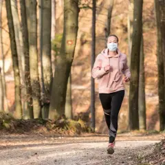 Femme courant en forêt avec un masque de protection.