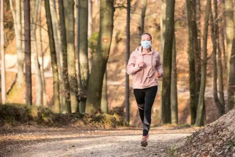 Femme courant en forêt avec un masque de protection.