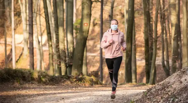Femme courant en forêt avec un masque de protection.